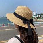 리본라피아햇 여성 밀짚모자 버킷햇을 착용한 모습, 넓은 챙과 리본 장식이 돋보이는 여름 휴양지 스타일