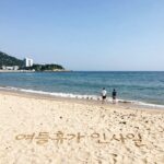 여름휴가 인사말 카드 이미지, 시원한 바다와 모래사장 위에 손글씨로 쓴 인사말이 적혀 있음